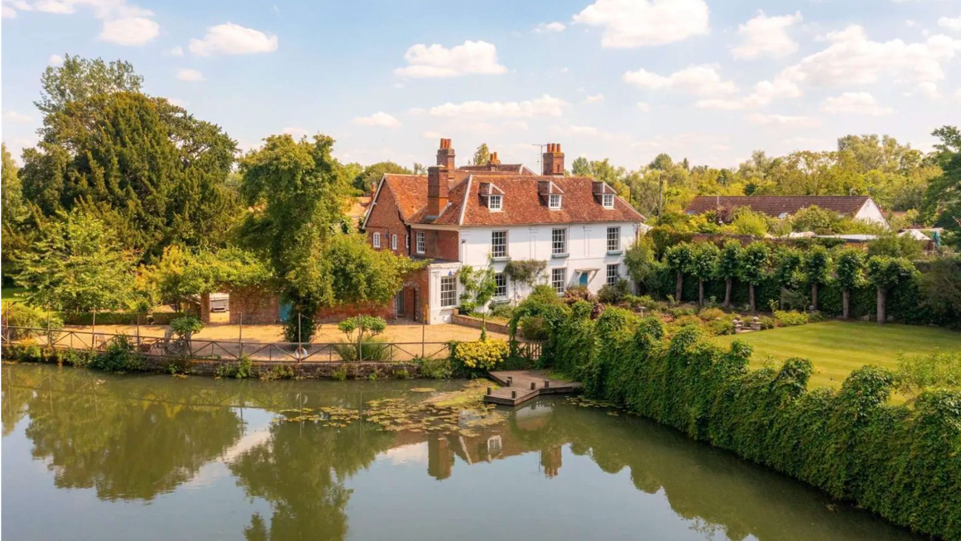 an image of the Grade II listed property which shows the house in the far right, the driveway and lake in front, and a lawn off to the side
