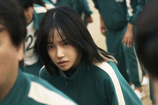 Jo Yu-ri as Jun-hee, standing among other players in green tracksuits, in 'Squid Game' season 2.