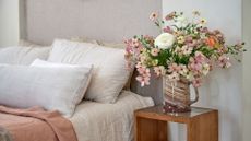 A close-up of a vase on a wood side table near a bed
