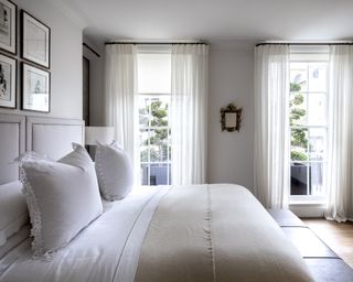 An example of bedroom curtain ideas showing a bedroom with white walls, sheets and curtains on a black rail