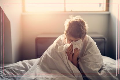 A young boy blowing his nose while wrapped in a duvet