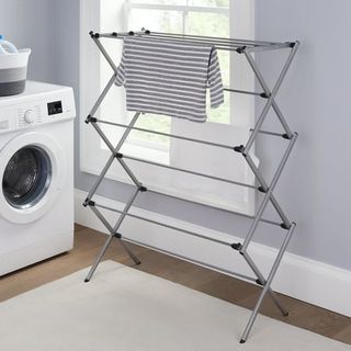 A gray metal concertina folding clothes drying rack in a blue laundry room with wooden floors and cream rug.