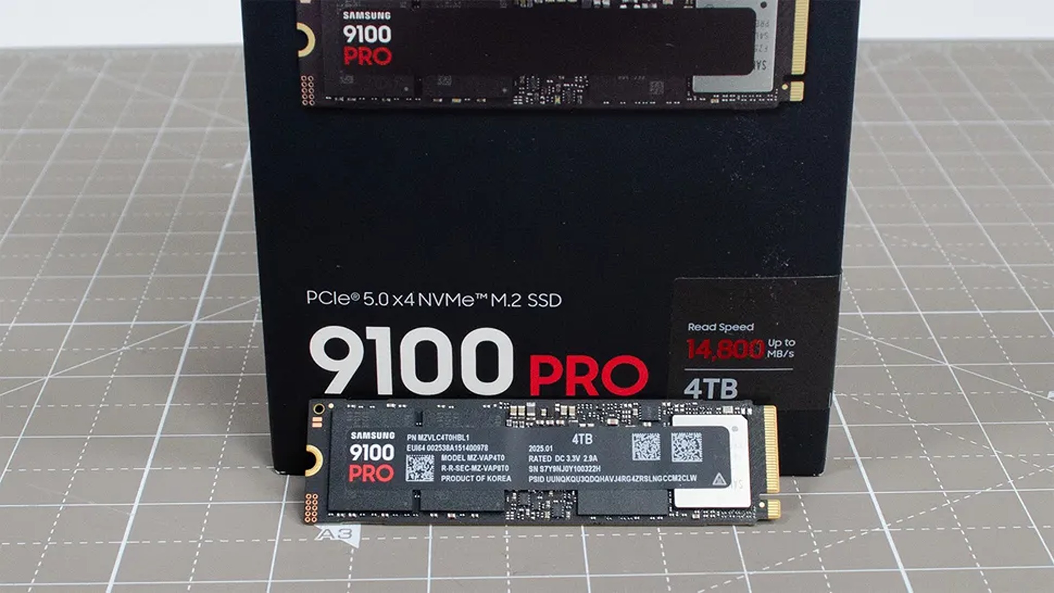 Close-up of a 4TB NVMe M.2 SSD resting against its black packaging box. The box highlights the model '9100 PRO' and a read speed of 14,800 MB/s
