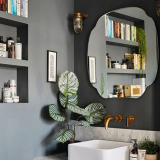 Bathroom detail with square basin on marble vanity unit and wall mirror on dark green walls