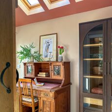 Home office with vintage wooden desk underneath sloped ceilings painted pink with row of skylights