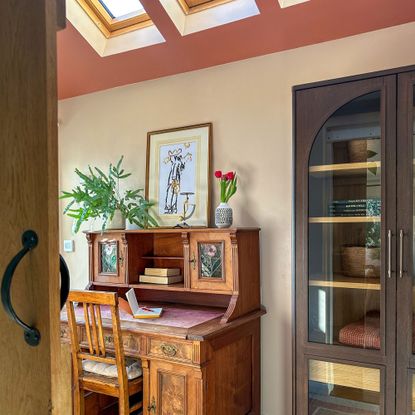 Home office with vintage wooden desk underneath sloped ceilings painted pink with row of skylights