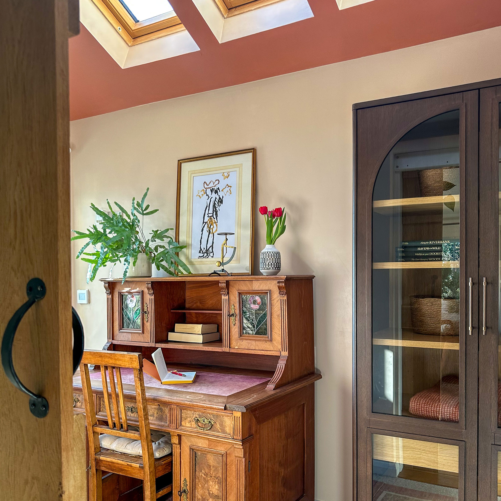 Home office with vintage wooden desk underneath sloped ceilings painted pink with row of skylights