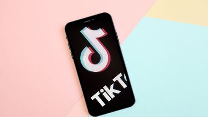 Is TikTok getting banned? Pictured: Cellphone on colorful background with TikTok logo