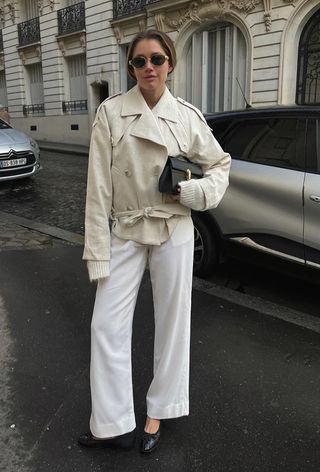 best cropped trench coat for women shown on a woman standing in the street wearing a light beige short trench with a white sweater, white jeans, and black ballet flats