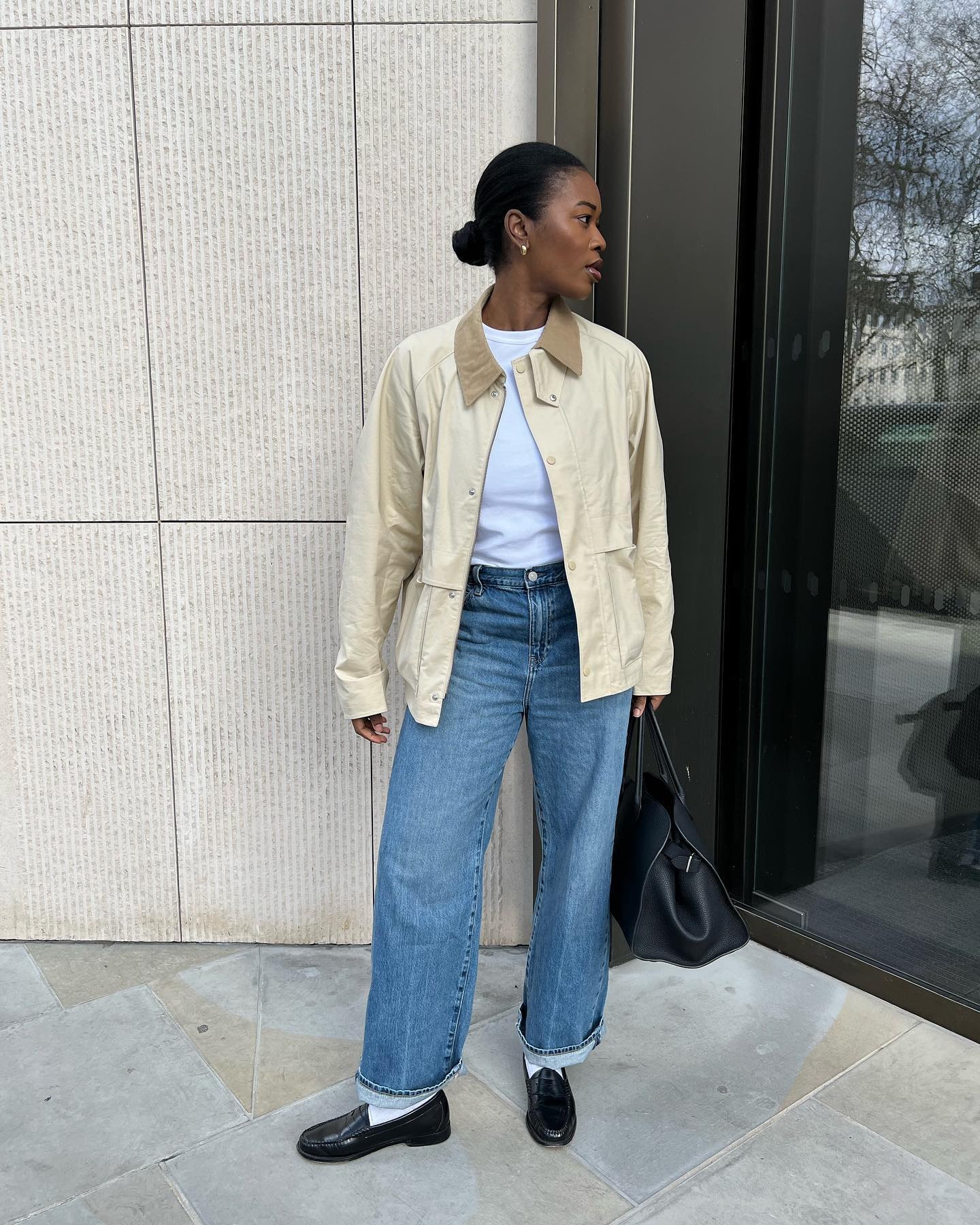 Influencer @nlmarilyn wears black leather flip-flops in London with mid-wash blue jeans, a light cream barn jacket and a fresh white tee.