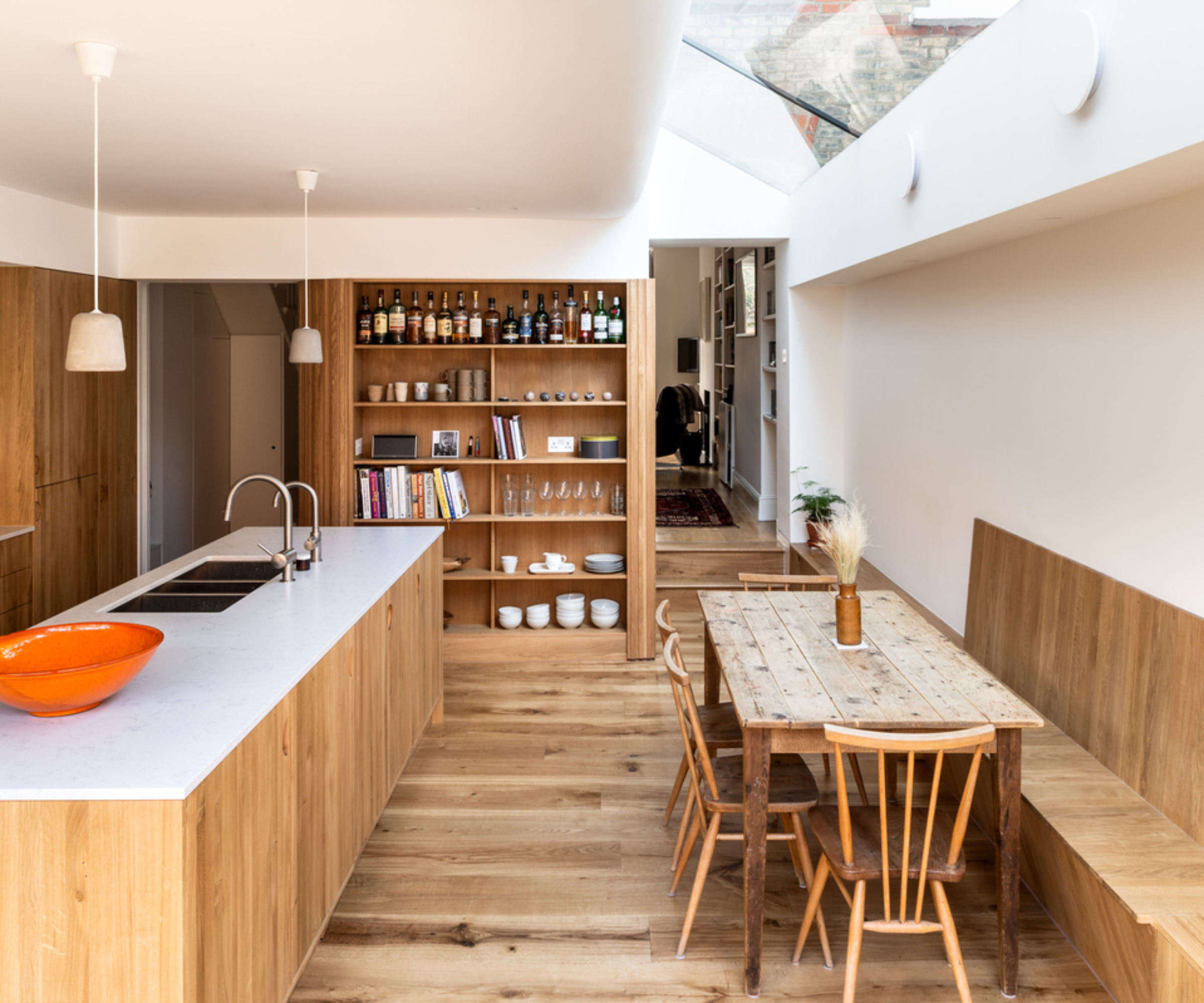 kitchen extension with curved ceiling section leading to large glass rooflight above built in kitchen banquette area finished in wood, with wood flooring and modern wood clad kitchen