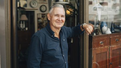 A mature male retiree stands outside an antique shop.