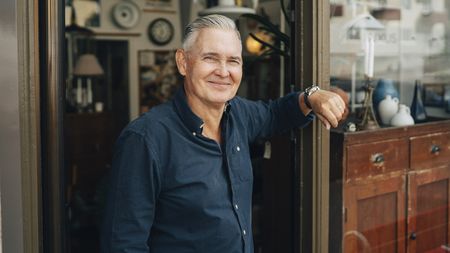 A mature male retiree stands outside an antique shop.