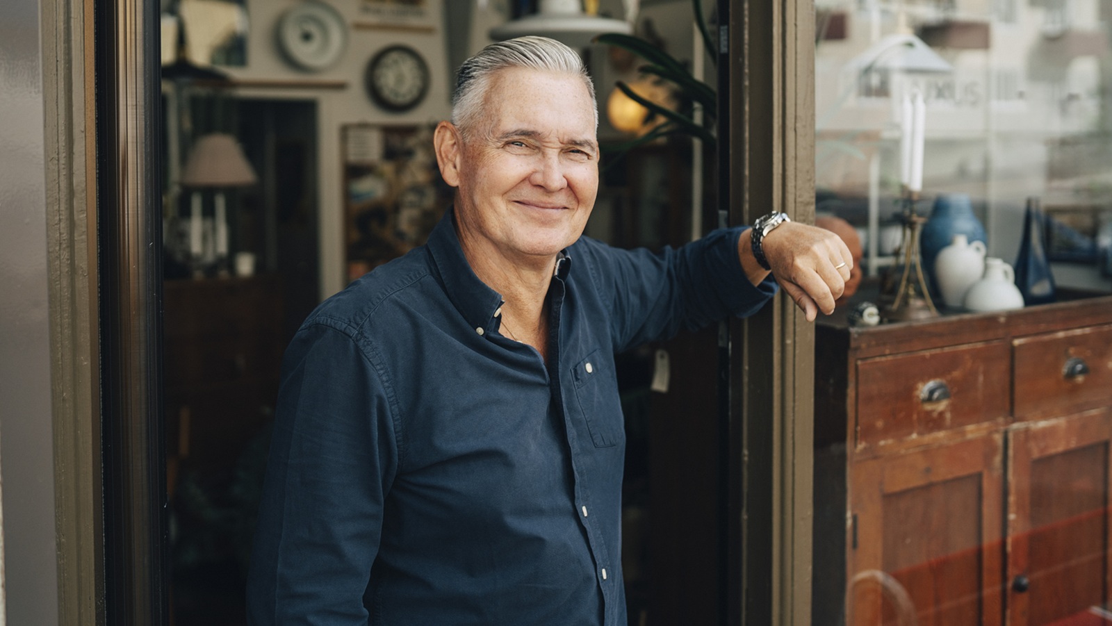 A mature male retiree stands outside an antique shop.