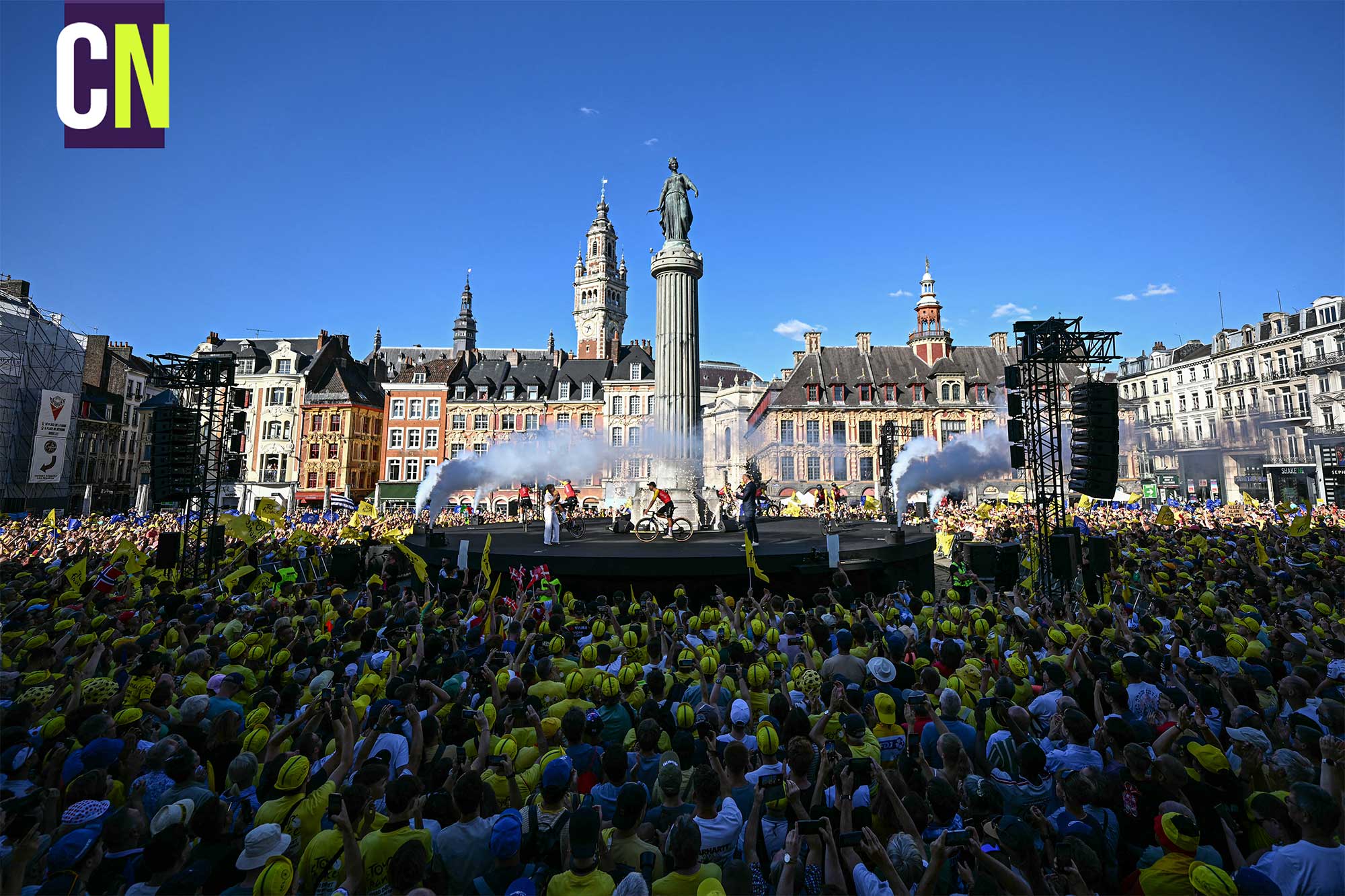 Fans hold yellow Tour de France flags ahead of the official teams presentation, days prior to the start of the 112th edition of the Tour de France cycling race, at Grand Place with a view of the Colonne de la Déesse monument and the the tower of the Vieille Bourse de Lille building, in Lille, northern France, on July 3, 2025. (Photo by Loic VENANCE / AFP) (Photo by LOIC VENANCE/AFP via Getty Images)