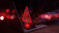 Cyber attacks concept image showing a red-colored warning symbol hovering above a laptop used by man in dark room.