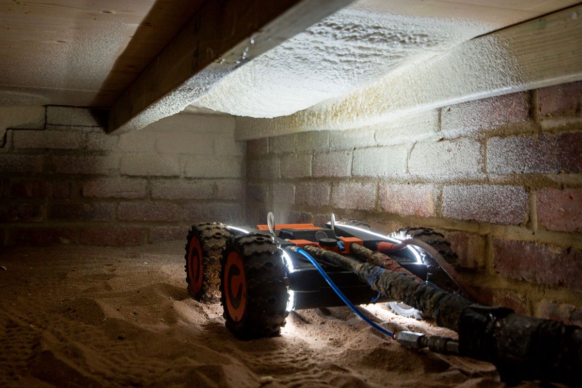 A Q-Bot robot sprays insulation under the floorboards of a property