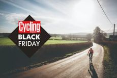 Black Friday image has the Cycling Weekly logo on a black diamond which says Black Friday in white. In the background is an image of a cyclist riding on an empty road, with a hedge to the right of the picture, with a green field behind and a wintery sunny sky above.