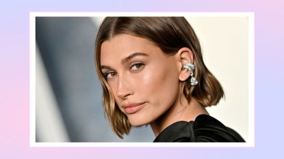 A close up of Hailey Bieber wearing a black dress and silver ear cuff as she attends the 2023 Vanity Fair Oscar Party hosted by Radhika Jones at Wallis Annenberg Center for the Performing Arts on March 12, 2023 in Beverly Hills, California. / in a pink and purple template