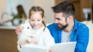 Father and daughter reading a book, daughter holding Pomeranian