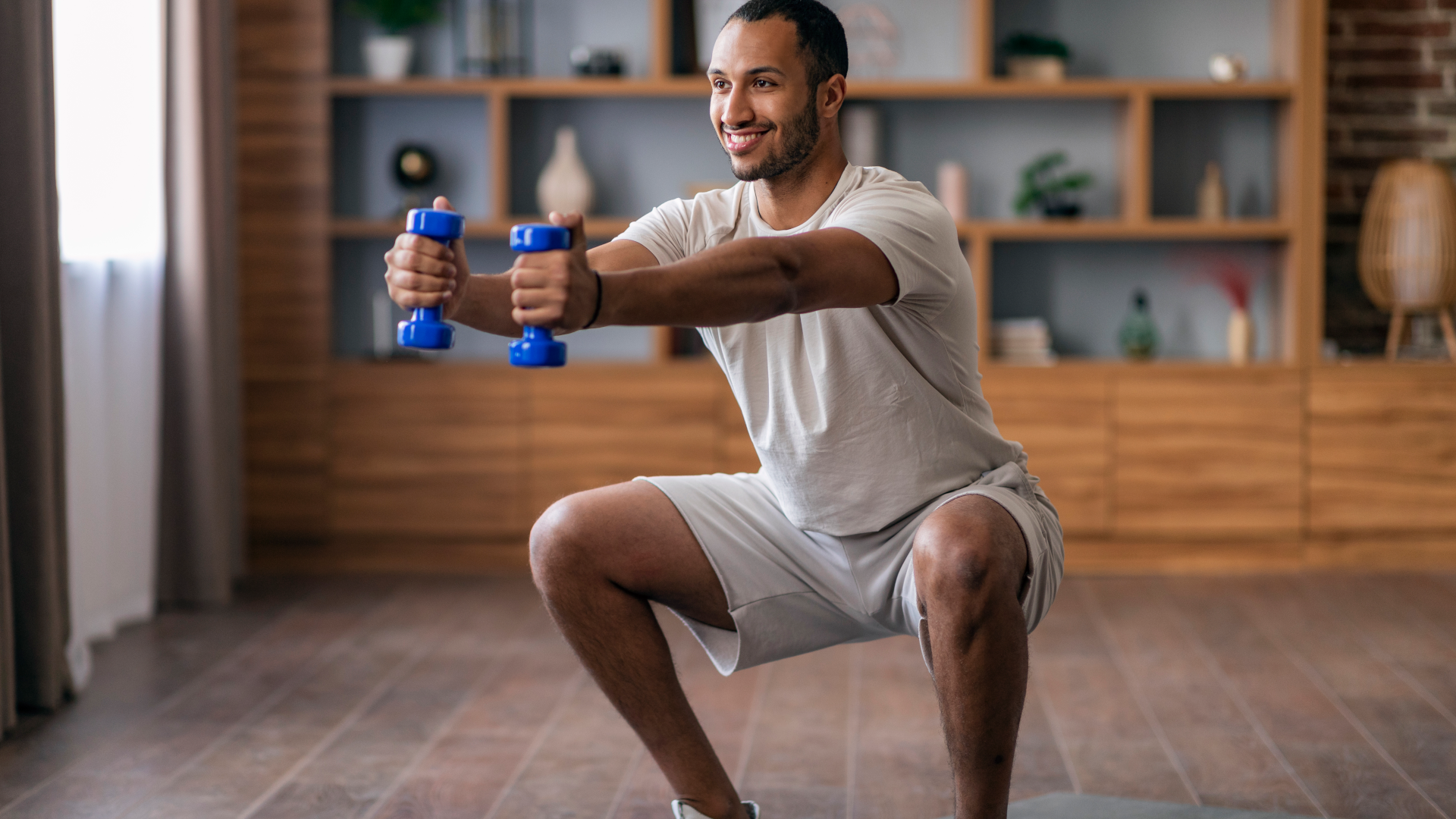 A man doing a squat with two small dumbbells in his living room