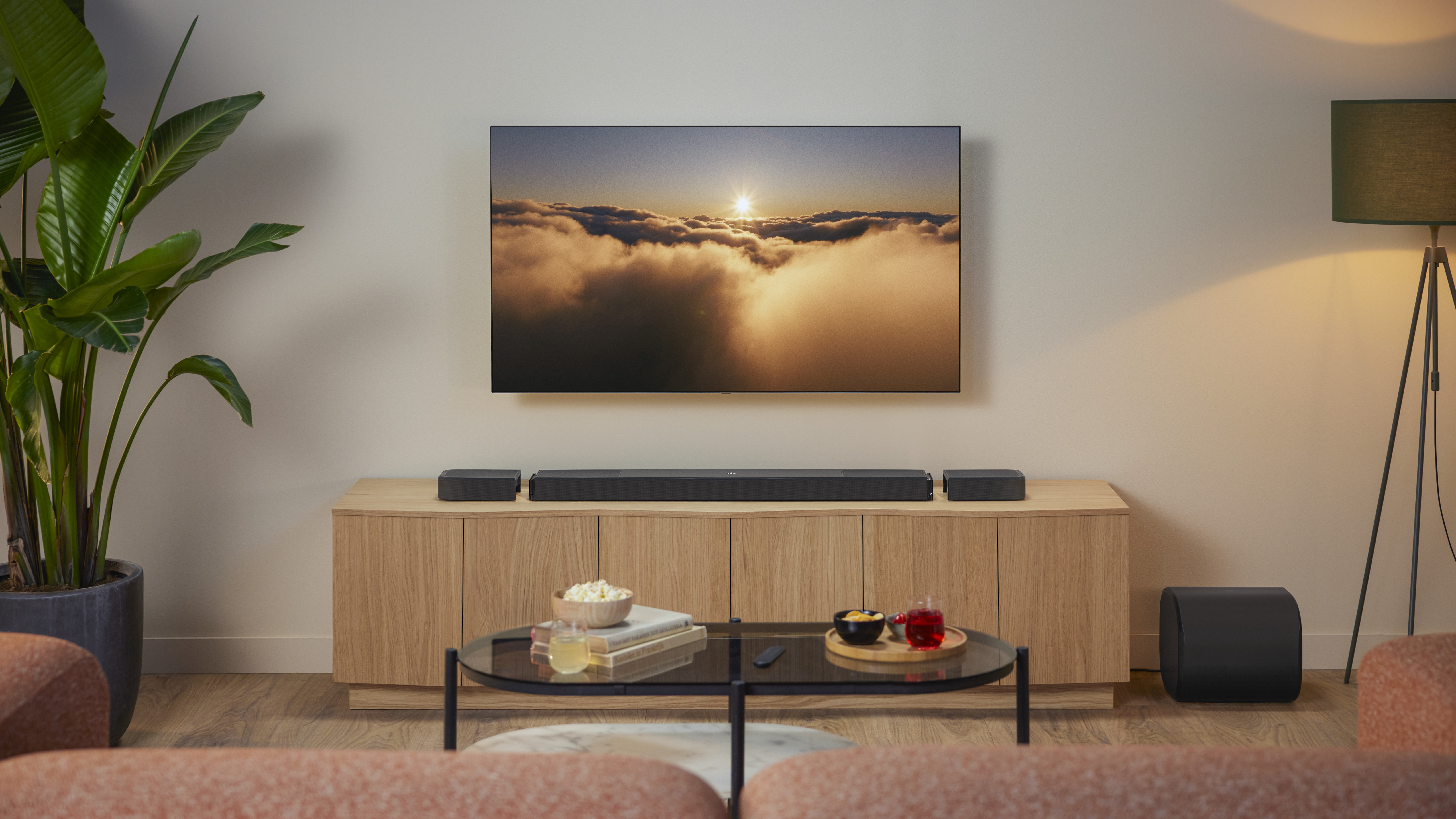 JBL Bar 1300MK2 in a modern living room sitting on a wooden media unit beneath a wall-mounted TV.