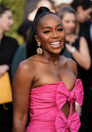 aja naomi king in a pink dress with her hair in a ponytail