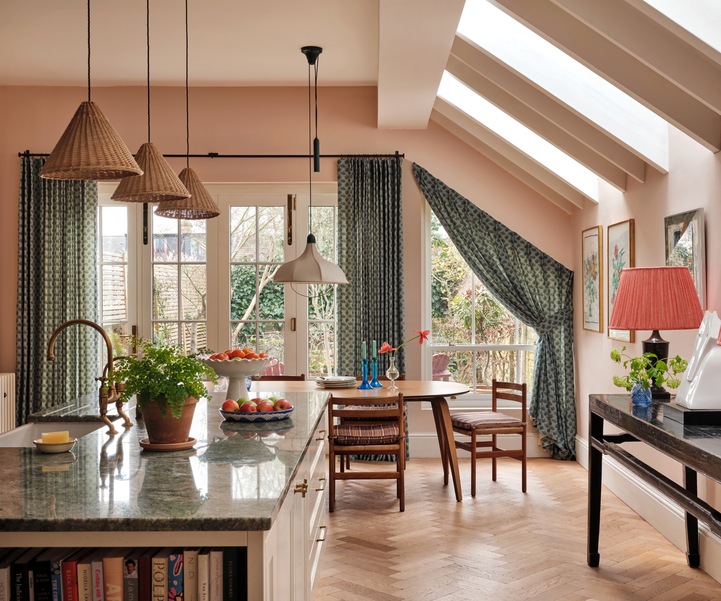 An open plan kitchen with green countertops, a wooden dining table, and pink walls