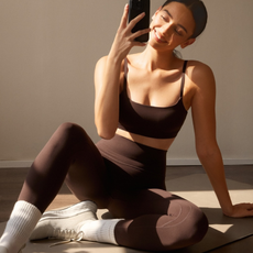 Woman taking a selfie wearing brown sports bra and brown leggings.