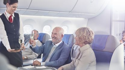 An older couple accept glasses of champagne from a flight attendant in first class.