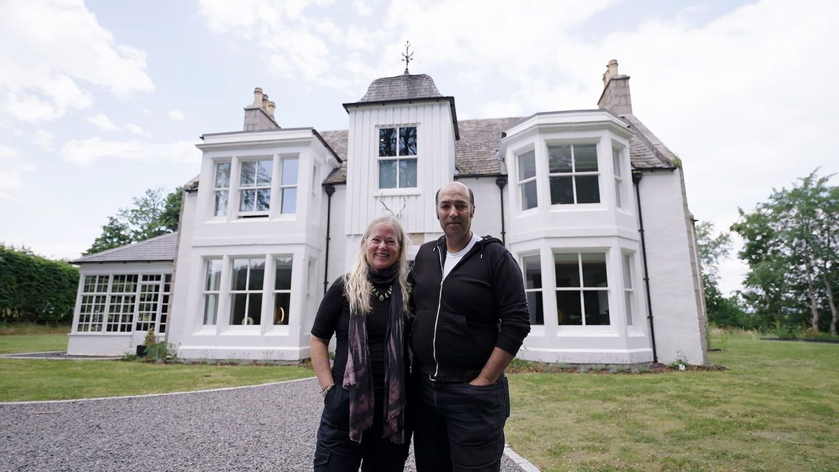 A couple standing in front of their white painted, two-storey house