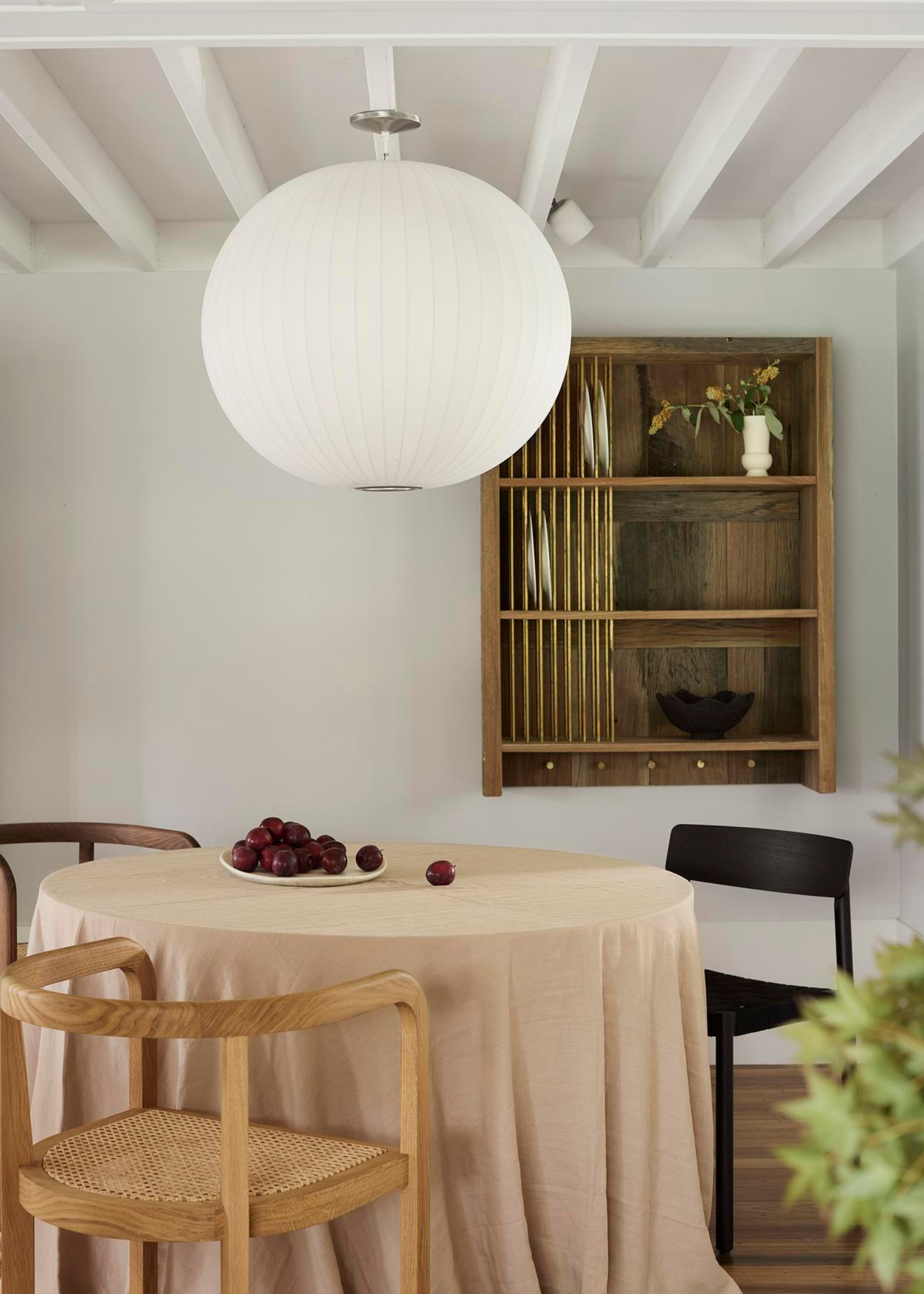 A white dining room with a wood storage cabinet, a circular table with a flowing tablecloth and mismatched chairs
