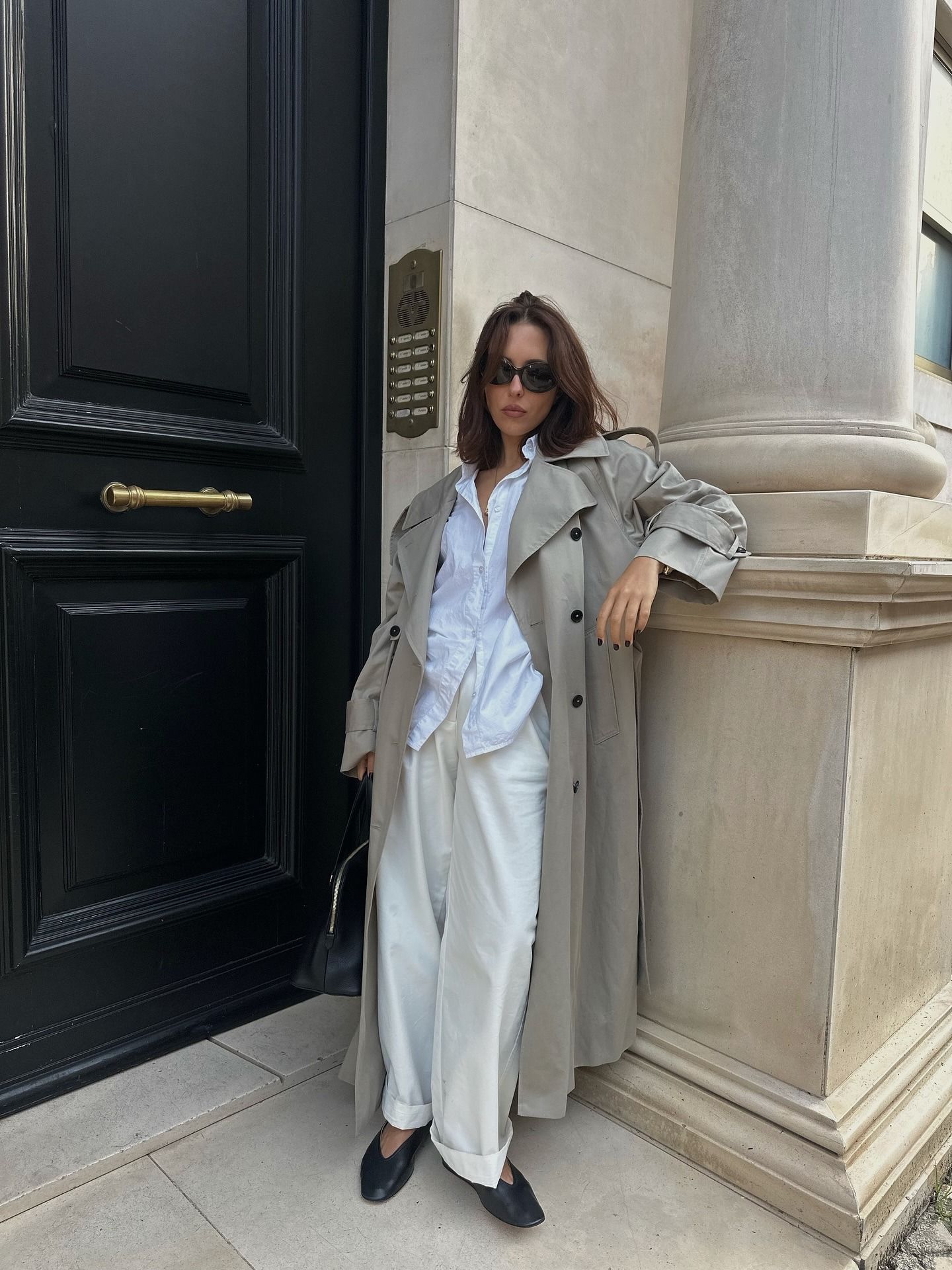 Influencer @​​deborabrosa wears white trousers with a grey trench coat and black soft leather ballet pumps.