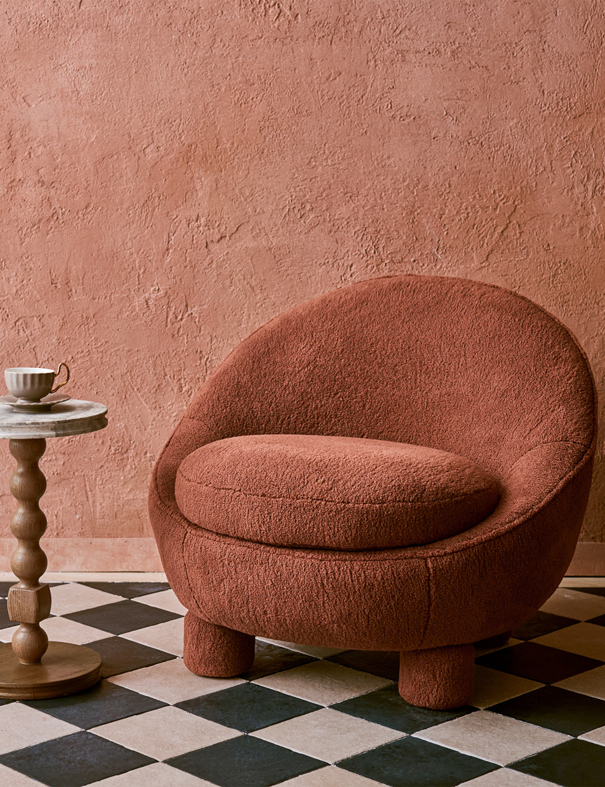 Vintage-inspired Rumi accent chair in rust styled alongside a sculptural drink table in room with a checkered floor
