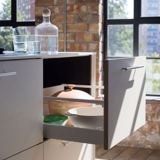 Open deep drawer in an industrial-style kitchen with exposed brick walls