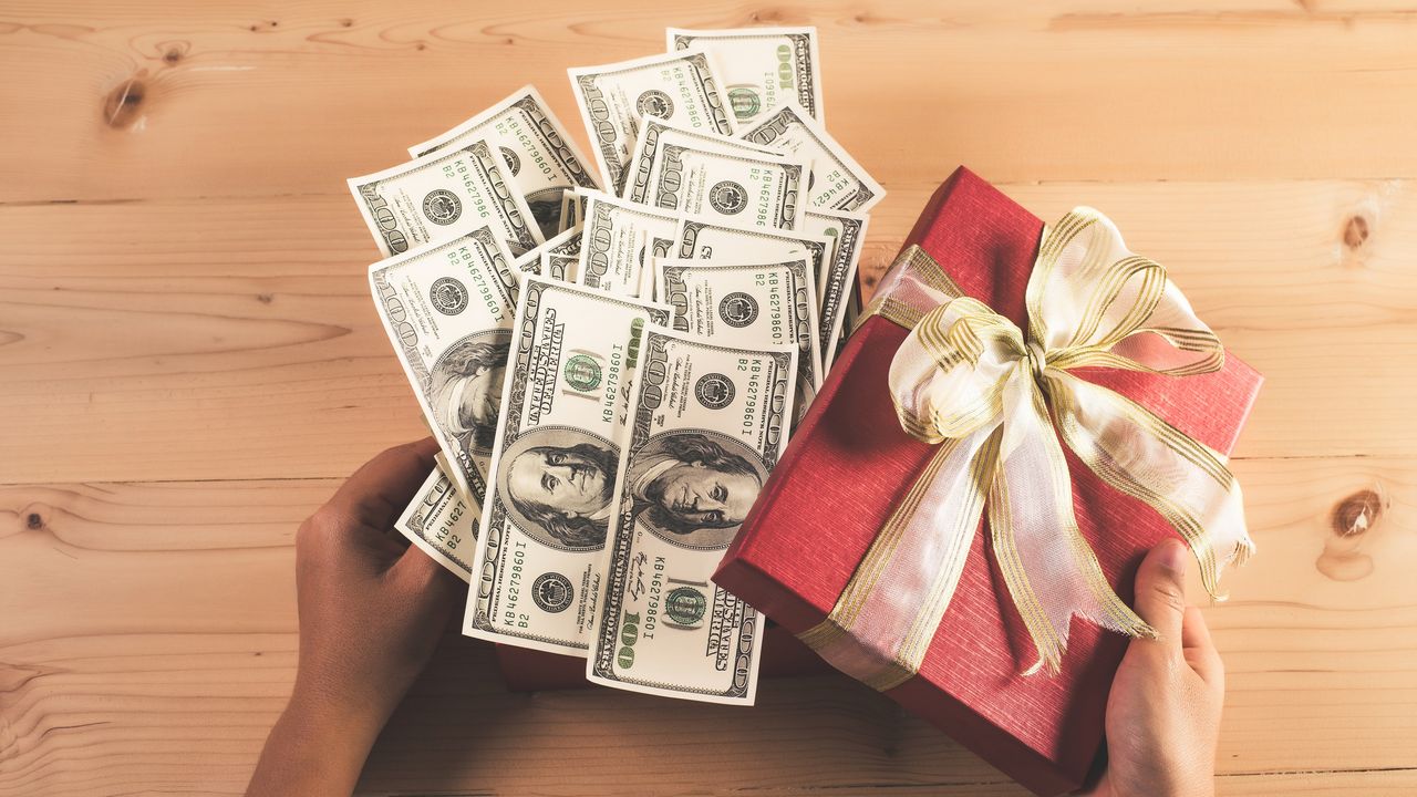 Hundred-dollar bills spill out of a festive gift box.