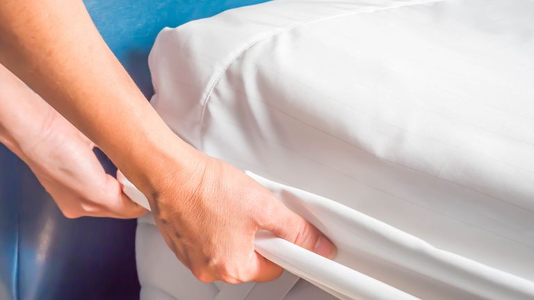 A pair of hands tucking a sheet over one of the best mattress protectors on a bed