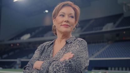 Kelli Finglass looks off to the side with her arms folded 