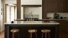 A kitchen with brown painted cabinets and white marble countertops. Gold fixtures