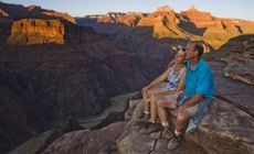 A mature couple sits looking out at the Grand Canyon.