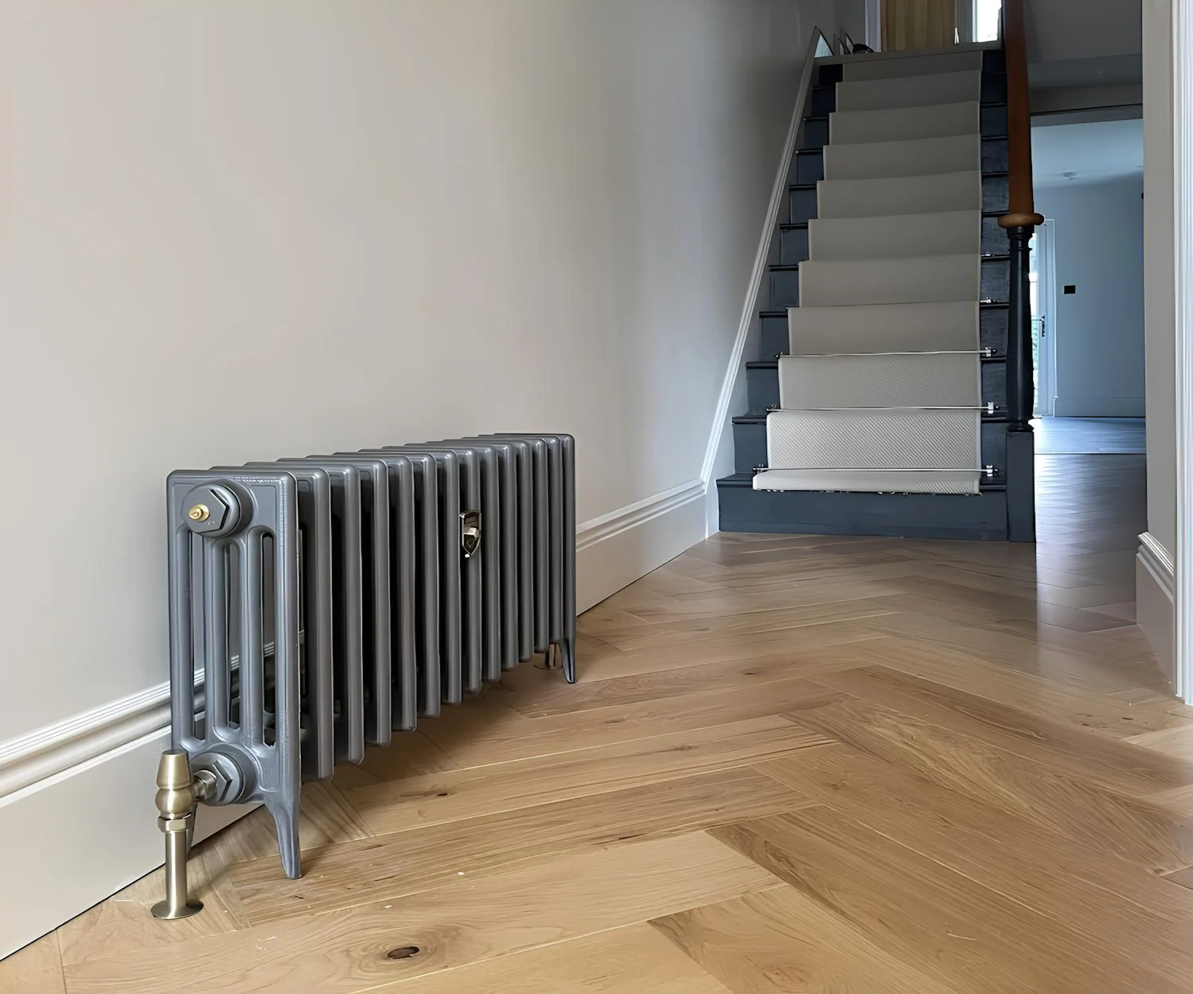 Grey column radiator in a hallway with parquet flooring and staircase with beige runner