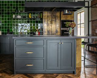 A black kitchen idea with black painted cabinets, green ceramic gloss tiles, and aged brass cabinet door