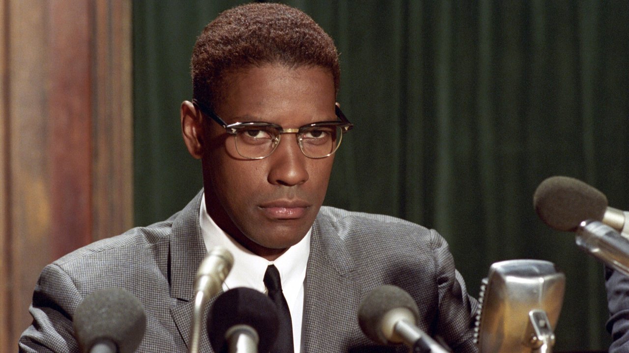 Denzel Washington sitting in front of several microphones in Malcolm X.