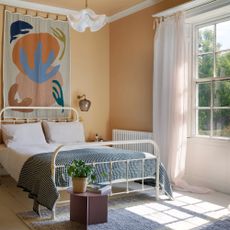 A peach-painted bedroom with a high ceiling and a window dressed with a white light curtain with top ties