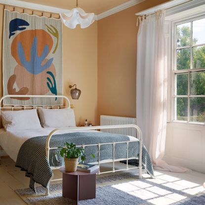 A peach-painted bedroom with a high ceiling and a window dressed with a white light curtain with top ties
