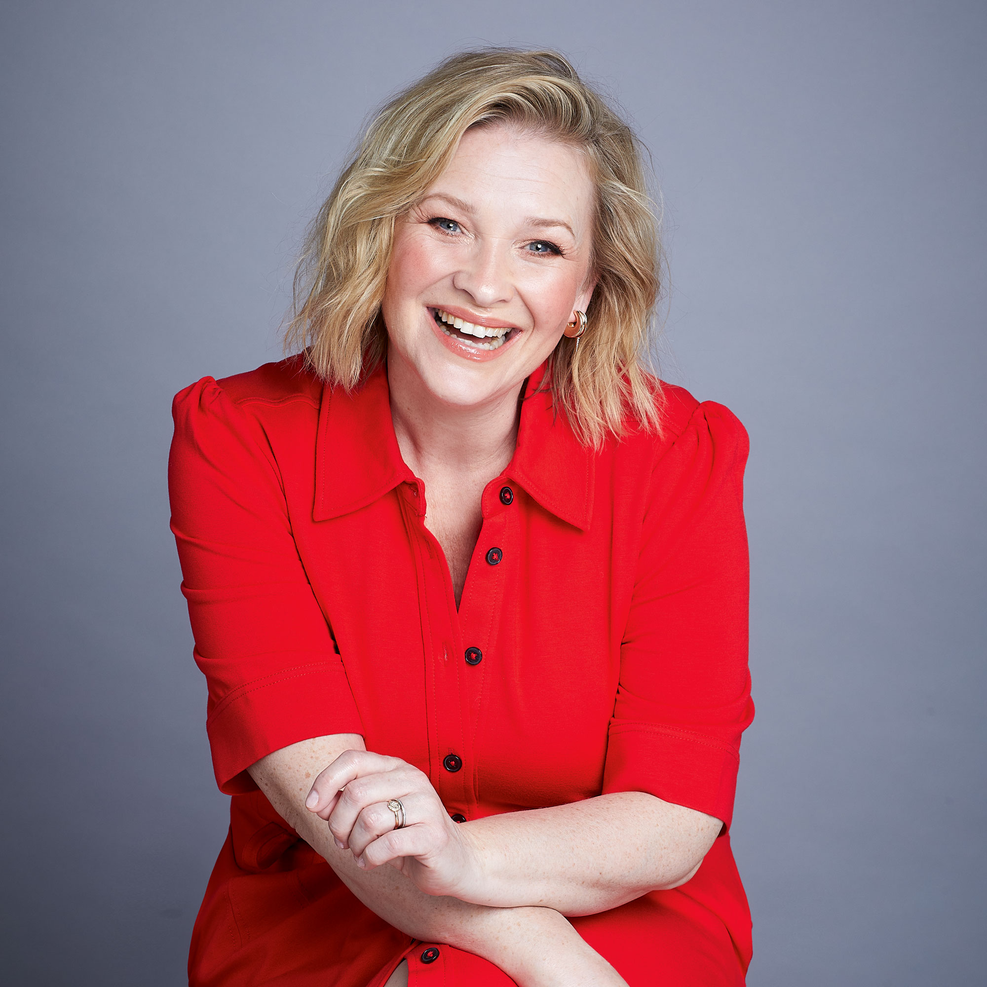 Joanna Page in a red outfit posing against a plain grey background
