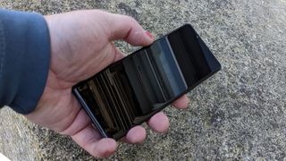 A black Sony Xperia 5 IV being held above and laid on a stony surface