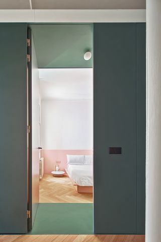 A bedroom with half pink walls and dark green doors