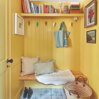 A yellow hallway with wood panelling, a built-in bench and top shelf and coat cooks shaped as birds