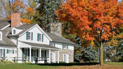 A large ranch style home. Green lawn and lots of orange autumn trees dropping leaves. 